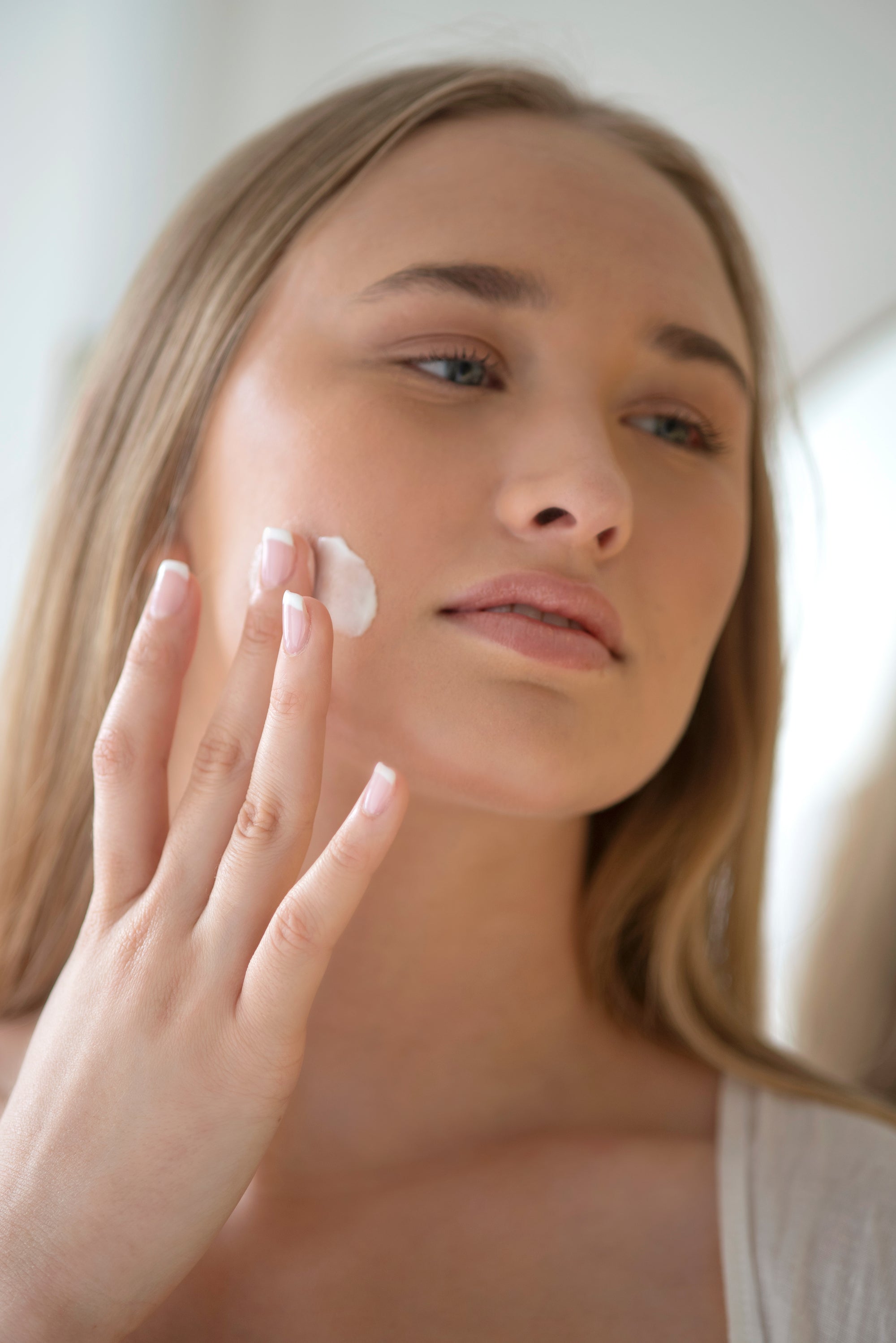 Woman applying cream to her face with a blurred background