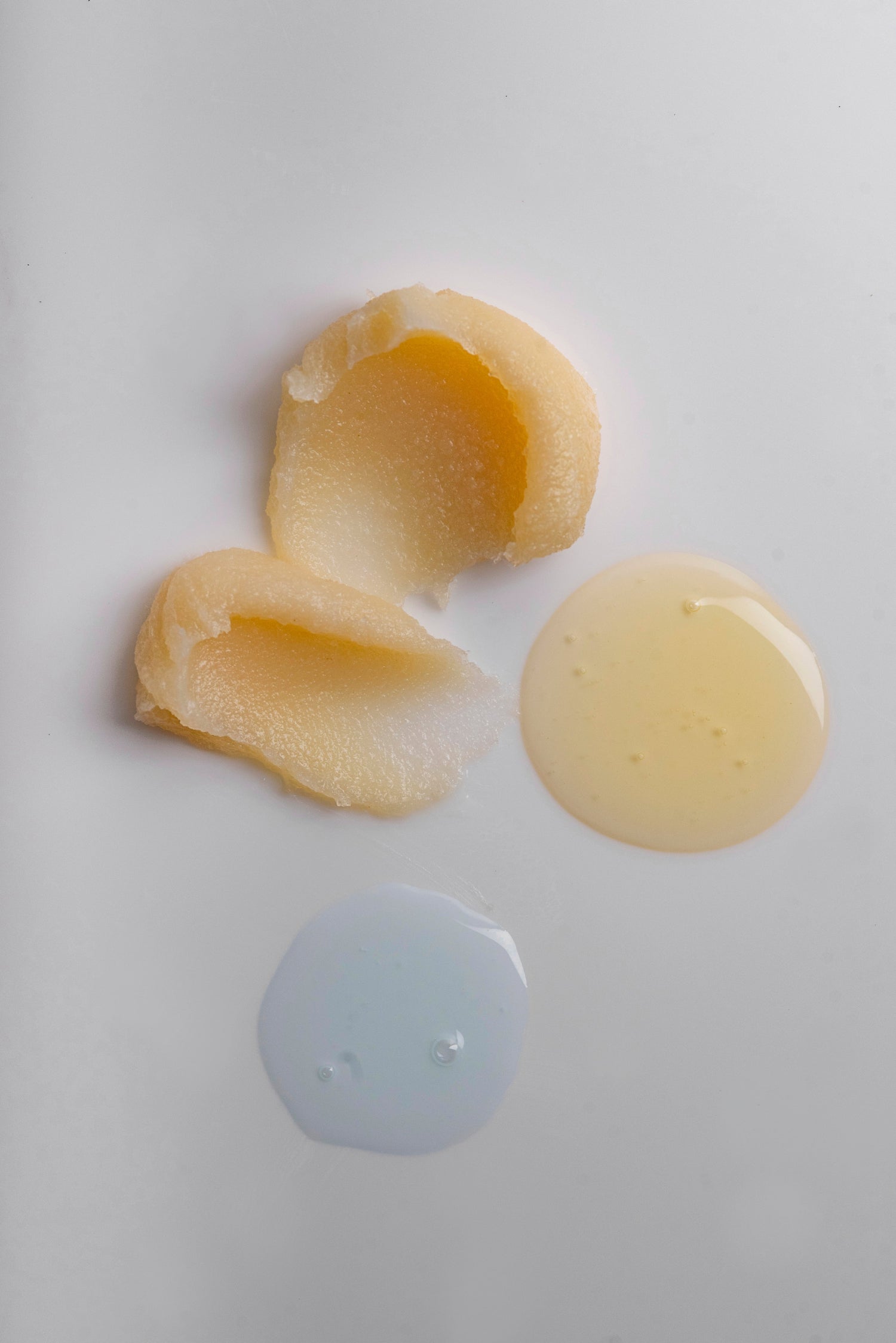 Two peeled potatoes on a white surface with a small puddle of liquid.