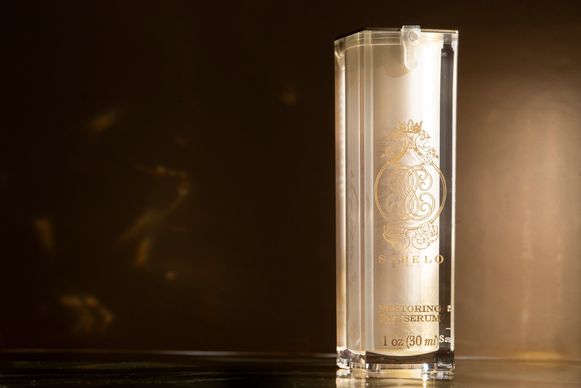 Clear skincare serum bottle with gold branding on a dark background